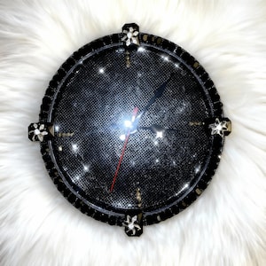 May include: A round black clock with a sparkling face and a black beaded border. The clock has black hands and a red second hand. Four decorative flower-shaped accents are placed around the clock face.
