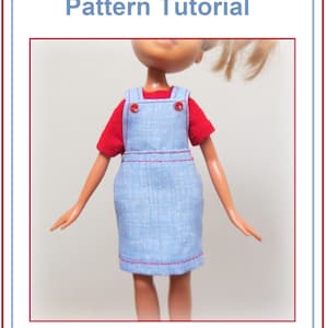 May include: A doll wearing a light blue overall jumper dress over a red t-shirt. The dress has red stitching and buttons. The text "OVERALL JUMPER Pattern Tutorial" and "by: Grace Filled Hands" are displayed.