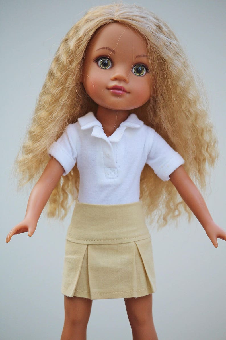 May include: A doll with long, curly blonde hair wearing a white collared shirt and a beige pleated skirt.