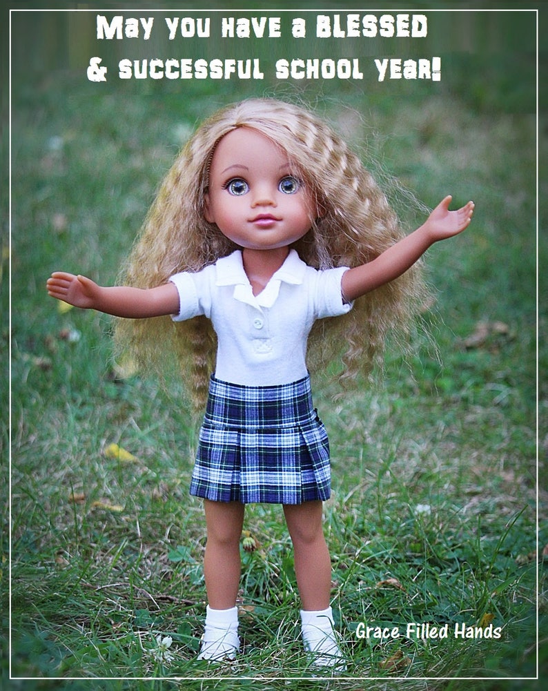 May include: A doll with long blonde hair wearing a white collared shirt and a blue and green plaid skirt. The doll is standing in a grassy field with her arms outstretched. The text "May you have a BLESSED & successful school year!" is at the top of the image. The text "Grace Filled Hands" is at the bottom of the image.