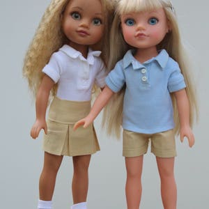 May include: Two dolls wearing school uniforms. One doll has blonde hair and is wearing a light blue polo shirt and khaki shorts. The other doll has brown hair and is wearing a white polo shirt and a khaki skirt. Both dolls are wearing white socks and shoes.
