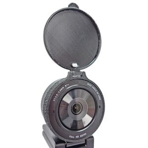 May include: A black Razer Kiyo Pro webcam with a wide-angle lens and a flip-up privacy cover. The lens has the text "F1.2/2.0 3.6MM 814 WIDE ANGLE AF LENS FULL HD 60FPS" printed around it.