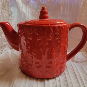May include: A red ceramic teapot with a floral design. The teapot has a lid with a knob on top.
