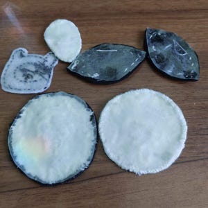 May include: A collection of six assorted fabric patches in various shapes including circles, ovals, and a character-like silhouette. The patches feature white, off-white, and dark grey colors with visible stitching along the edges and adhesive backings.