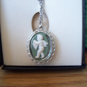 Puede incluir: Un collar de cadena de plata con un colgante de camafeo verde que presenta un querubín blanco tocando un instrumento musical.