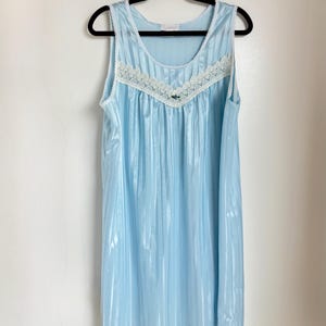 Könnte beinhalten: Ein hellblaues, ärmelloses Nachthemd mit weißer Spitzenborte und einem kleinen Blumenapplikation. Das Nachthemd hat vertikale Streifen.