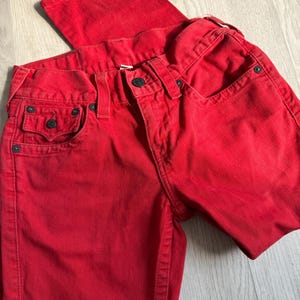 以下が含まれることがあります： 鮮やかな赤色のデニムジーンズ。クラシックな5ポケットのデザイン。ボタンとジッパーで開閉し、ベルトループとリベットが付いています。生地は中程度の厚さで、普段使いに適しています。