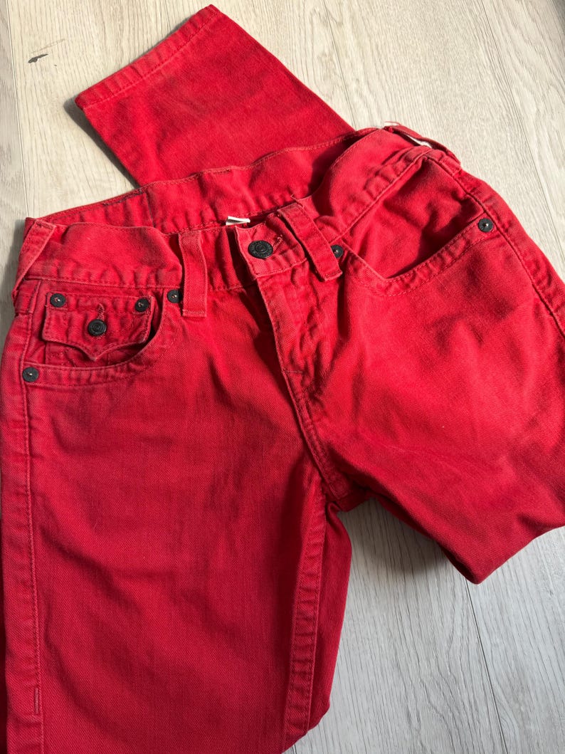 以下が含まれることがあります： 鮮やかな赤色のデニムジーンズ。クラシックな5ポケットのデザイン。ボタンとジッパーで開閉し、ベルトループとリベットが付いています。生地は中程度の厚さで、普段使いに適しています。