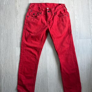 以下が含まれることがあります： 鮮やかな赤色のデニムジーンズ。クラシックな5ポケットのデザイン。ボタンとジッパーで開閉し、丈夫で耐久性のある素材で作られています。無地で、ストレートレッグフィットです。
