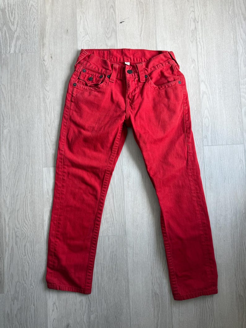 以下が含まれることがあります： 鮮やかな赤色のデニムジーンズ。クラシックな5ポケットのデザイン。ボタンとジッパーで開閉し、丈夫で耐久性のある素材で作られています。無地で、ストレートレッグフィットです。