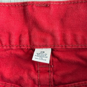 以下が含まれることがあります： 赤いデニム生地のクローズアップ。ステッチと白いタグが見えます。タグには「28 MADE IN MEXICO FABRIQUE EN MEXIQUE」と書かれています。生地はジーンズのようです。