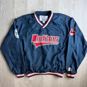 Könnte beinhalten: Ein marineblauer Pullover mit langen Ärmeln und dem in Rot und Weiß gestickten Wort Indians auf der Brust. Die Jacke hat einen V-Ausschnitt mit rot-weißen Streifen, ein Starter-Logo am linken Ärmel und ein Team-Abzeichen auf der rechten Seite.