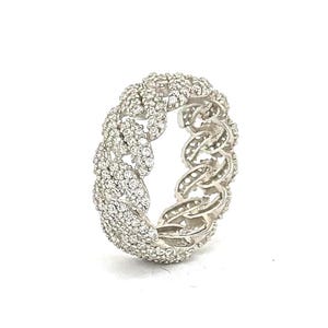 Puede incluir: Un anillo plateado con un diseño de eslabones de cadena, incrustado con numerosas piedras preciosas pequeñas y transparentes. El anillo se presenta sobre un fondo blanco, resaltando sus intrincados detalles y su apariencia brillante.