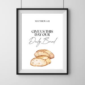 May include: A framed print with the text "MATTHEW 6:11" and "GIVE US THIS DAY OUR Daily Bread." The image features a watercolor illustration of sliced bread. The frame is black.