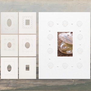 May include: A collection of white rectangular cardstock frames featuring embossed shell and geometric border patterns. One large frame displays a central rectangular cutout containing a photographic image of a white pearl inside an open oyster shell.