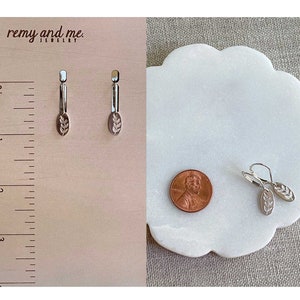 Op de afbeelding: Zilverkleurige oorbellen met een bladmotief. De oorbellen worden getoond met een cent en een liniaal. De oorbellen zijn ongeveer 2.5 cm lang. De merknaam "remy and me" is zichtbaar in de afbeelding.