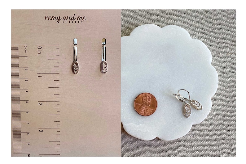 Op de afbeelding: Zilverkleurige oorbellen met een bladmotief. De oorbellen worden getoond met een cent en een liniaal. De oorbellen zijn ongeveer 2.5 cm lang. De merknaam "remy and me" is zichtbaar in de afbeelding.