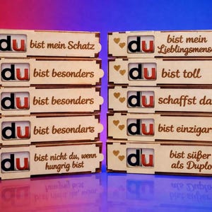 Könnte beinhalten: Holzkisten mit dem Wort "du" in Rot und Schwarz, kombiniert mit deutschen Sätzen wie "bist mein Schatz" und "bist besonders". Jede Kiste hat herzförmige Akzente, ideal zum Verschenken.
