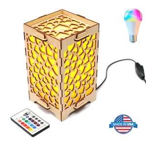 May include: A wooden cube-shaped lamp with heart-shaped cutouts, illuminated with a warm yellow light. Includes a remote control and a color-changing LED light bulb. The lamp is connected to a power cord and features a "MADE IN USA" sticker.