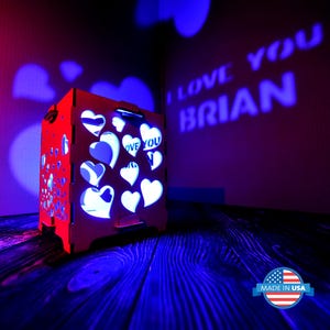 May include: A red wooden box with a heart-shaped design and a light inside that projects the words "I love you Brian" onto the wall. The box is sitting on a wooden surface. Made in USA.
