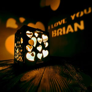 May include: A wooden box with a heart-shaped design that projects the words "I love you Brian" onto a wall. The box is lit from within, creating a warm glow.