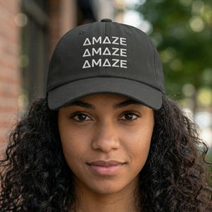 Op de afbeelding: Zwarte baseball cap met het woord "AMAZE" drie keer in het wit gedrukt. De cap heeft een gebogen klep en een klassiek zes-panelen ontwerp. De hoed is gemaakt van een duurzame stof en is geschikt voor dagelijks gebruik.