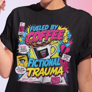 Woman wearing black Fueled by Coffee and Fictional Trauma bookish graphic tee, colorful retro comic style print, book lover gift, pink gradient background