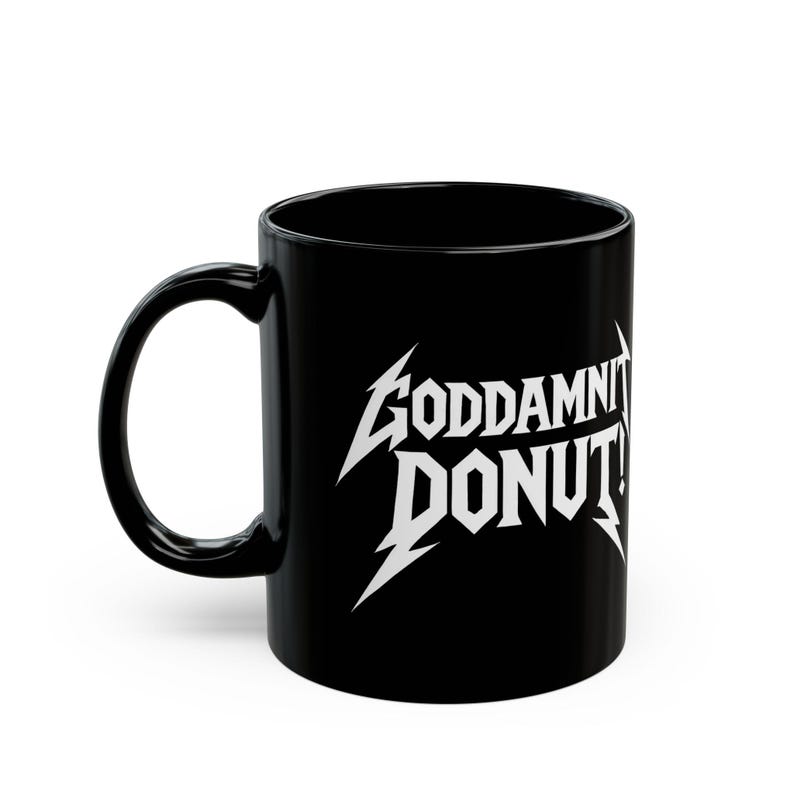 Black ceramic mug with bold white text in a Metallica-style font that reads “Goddamnit Donut,” inspired by Dungeon Crawler Carl. The mug is set on a modern kitchen counter, perfect for fans of LitRPG, Princess Donut, and Matt Dinniman's cult book series. Ideal for coffee or tea lovers who enjoy a mix of humor, chaos, and fandom in their daily routine.
