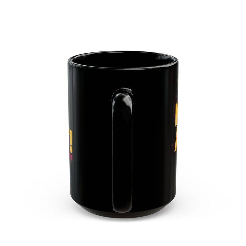 May include: A black ceramic coffee mug with a large handle. The mug has yellow and pink text on the side. The mug is a standard size for hot beverages.