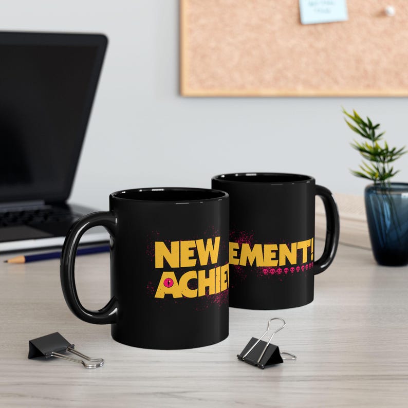 Two black ceramic mugs with yellow New Achievement text and pink donut graphic on desk, Dungeon Crawler Carl LitRPG fantasy book lover gift coffee cup