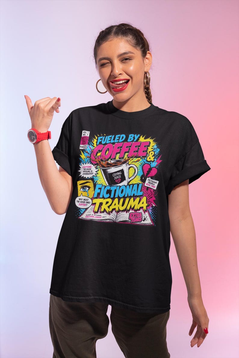 Woman wearing black Fueled by Coffee and Fictional Trauma bookish graphic tee, colorful retro comic style print, book lover gift, pink gradient background