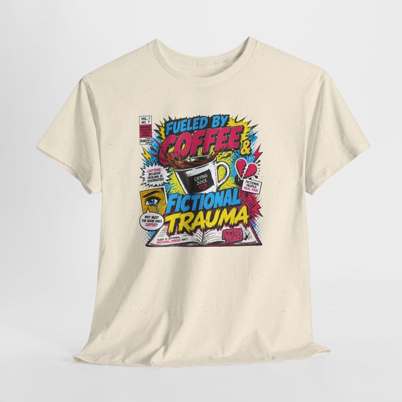 Pu&ograve; includere: T-shirt color crema con grafica in stile fumetto. Il design include una tazza di caff&egrave;, un cuore spezzato e le parole "Fueled by Coffee & Fictional Trauma". Il testo aggiuntivo include "Crying Juice" e "Vol. 1 n. 7."