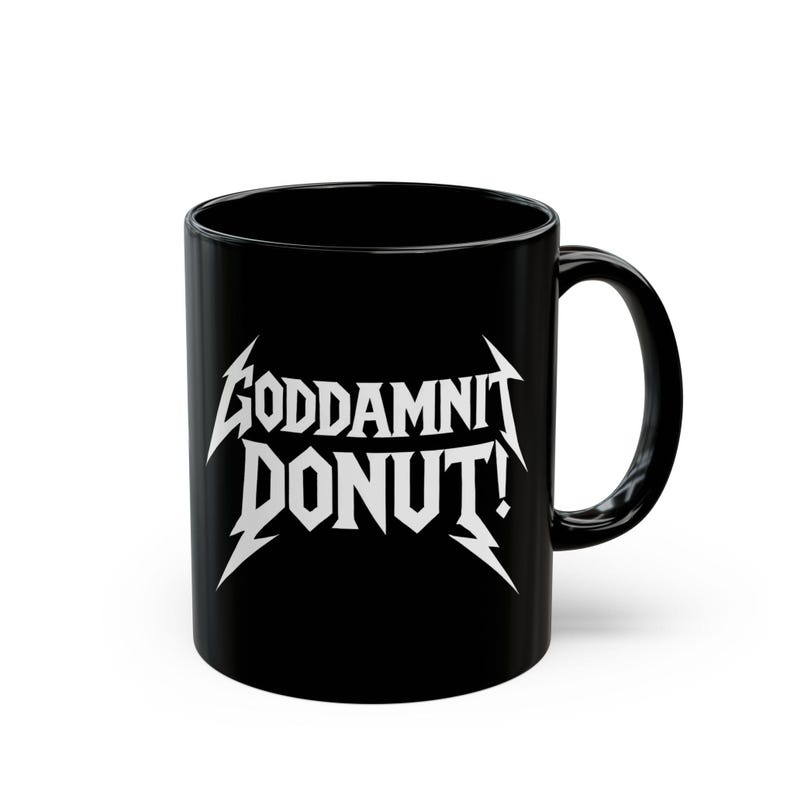 Black ceramic mug with bold white text in a Metallica-style font that reads “Goddamnit Donut,” inspired by Dungeon Crawler Carl. The mug is set on a modern kitchen counter, perfect for fans of LitRPG, Princess Donut, and Matt Dinniman's cult book series. Ideal for coffee or tea lovers who enjoy a mix of humor, chaos, and fandom in their daily routine.