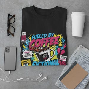 Aesthetic flat lay of black Fueled by Coffee and Fictional Trauma bookish tee with glasses, notebook, phone and earphones, bookish gift idea styling