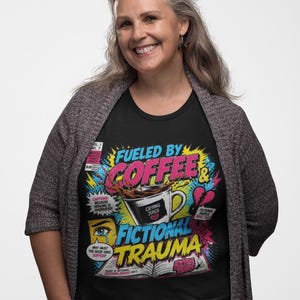 Woman wearing black Fueled by Coffee and Fictional Trauma bookish tee with grey cardigan, colorful comic print, funny reader gift shirt for book lovers