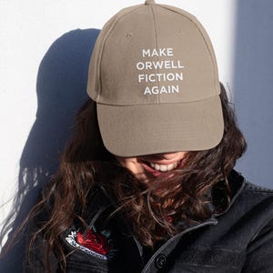 May include: A brown baseball cap with white embroidered text that reads "MAKE ORWELL FICTION AGAIN".