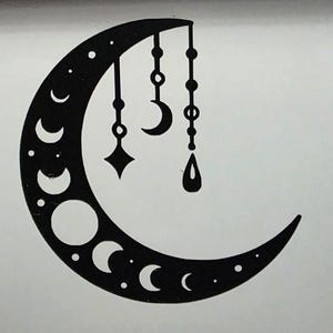 Puede incluir: Dise&ntilde;o de luna creciente negra con fases y colgantes. La luna presenta varias formas de media luna y puntos, con tres colgantes colgantes: un diamante, una media luna y una gota. El dise&ntilde;o est&aacute; sobre un fondo blanco.