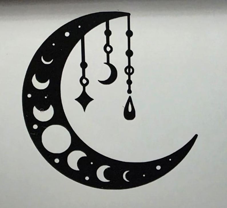 Puede incluir: Dise&ntilde;o de luna creciente negra con fases y colgantes. La luna presenta varias formas de media luna y puntos, con tres colgantes colgantes: un diamante, una media luna y una gota. El dise&ntilde;o est&aacute; sobre un fondo blanco.