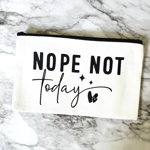 May include: A white canvas zippered pouch with the text "Nope Not Today" in black, along with two small stars and a heart design. The pouch has a black zipper and trim.