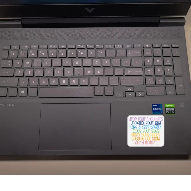 May include: A gray laptop computer with a sticker that reads "drop your shoulders, unclench your jaw, take a deep breath, close your eyes, relax your hands, breathe out slow, take a moment".