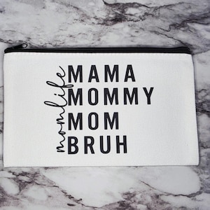 May include: White canvas zippered pouch with black text that reads "mama life mommy mom bruh".