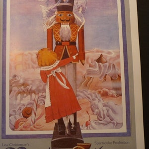 May include: A vintage poster advertising a production of The Nutcracker. The poster features a colorful illustration of a young girl in a red dress standing next to a large, wooden nutcracker. The text on the poster reads "Low Christensen's Nutcracker Spectacular Production".
