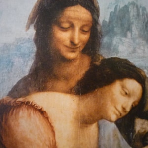 May include: A painting of two women, one with long dark hair and a light blue dress, the other with long brown hair and a brown dress. The woman in the blue dress is holding the other woman's head in her hands.