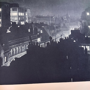 May include: A black and white photograph of a city skyline at night. Buildings with lit windows are visible, along with rooftops and chimneys. The image has a vintage, noir aesthetic.