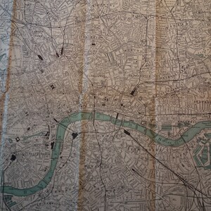 Könnte beinhalten: Eine Vintage-Karte von London, England, die die Straßen und Sehenswürdigkeiten der Stadt zeigt. Die Karte ist auf cremefarbenem Papier gedruckt und zeigt eine grüne Linie, die die Themse darstellt.