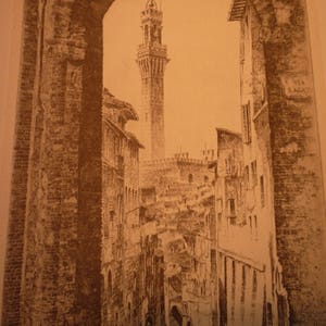 May include: A black and white photo of a narrow street in a European city. The street is lined with tall buildings, and there is a tower in the distance. The text "VIA SAGLARIO" is visible on the side of one of the buildings.