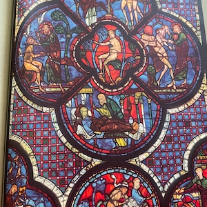 Puede incluir: Una ventana de vidriera que representa escenas de la Biblia. El panel superior muestra a Dios creando el mundo, el panel del medio muestra a Adán y Eva siendo tentados por la serpiente, y el panel inferior muestra la expulsión del Jardín del Edén.