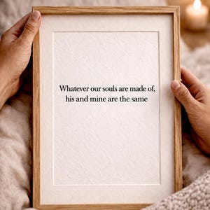Puede incluir: Una impresión enmarcada con un marco de madera clara, sostenida por manos. La impresión presenta la cita: "Whatever our souls are made of, his and mine are the same" en negro sobre un fondo blanco.