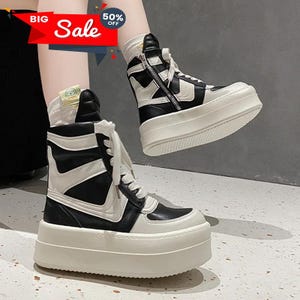 May include: Black and white platform sneakers with a high-top design. The sneakers feature a thick, off-white sole and a side zipper. The image also includes text that says "Big Sale" and "50% Off".