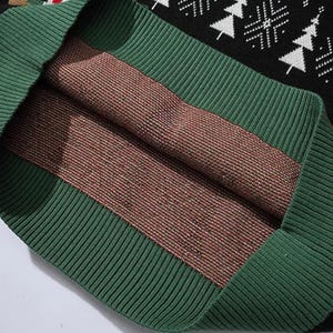 May include: Close-up of the inside of a black and green sweater with a red and white snowflake pattern. The sweater is made of a soft, knitted fabric.